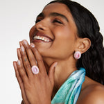 Smiling model wearing Soru Jewellery large pink stud earrings surrounded by crystals and a matching ring