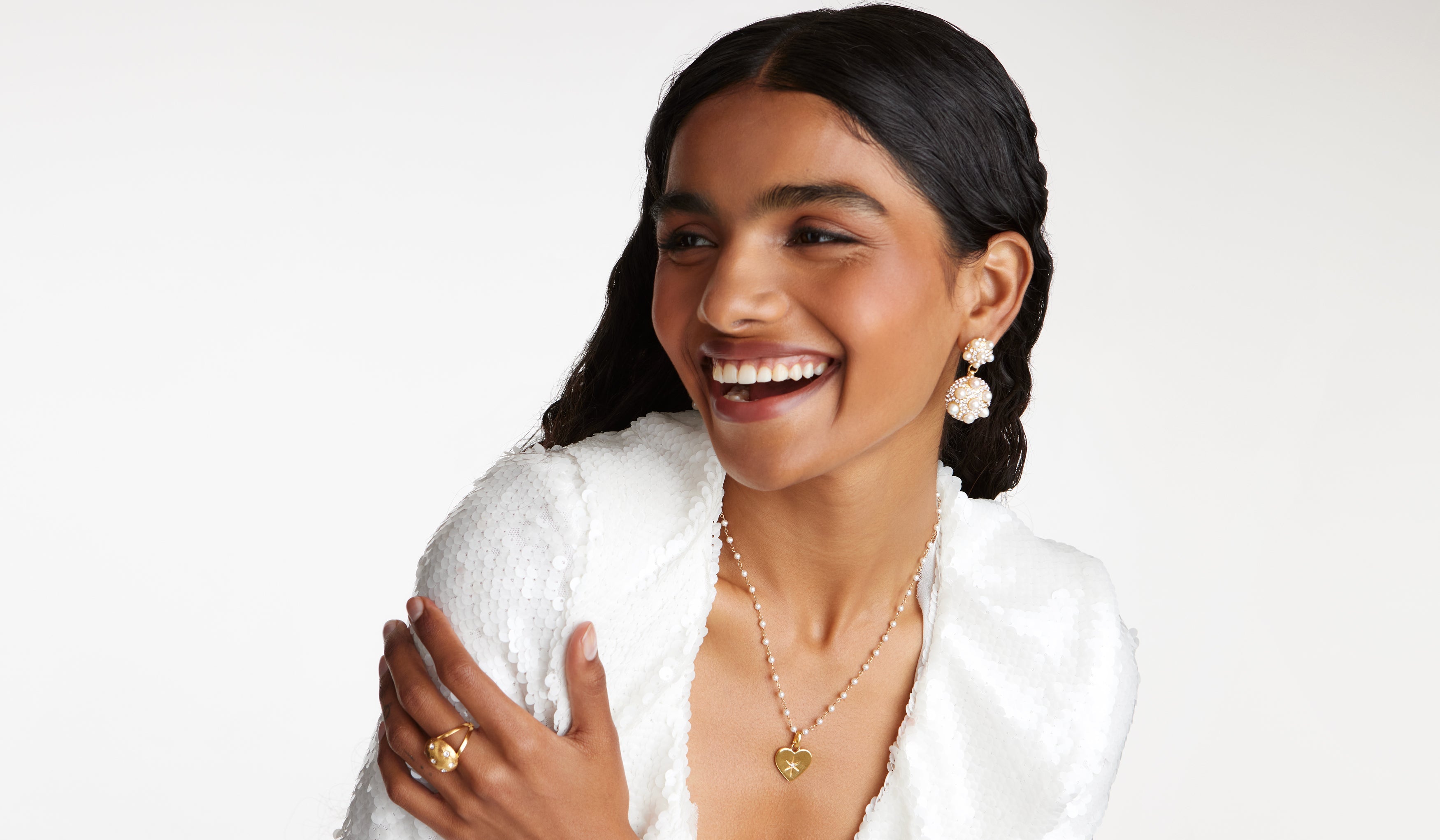 model laughing wearing pearl earrings and necklace and a white sequin dress