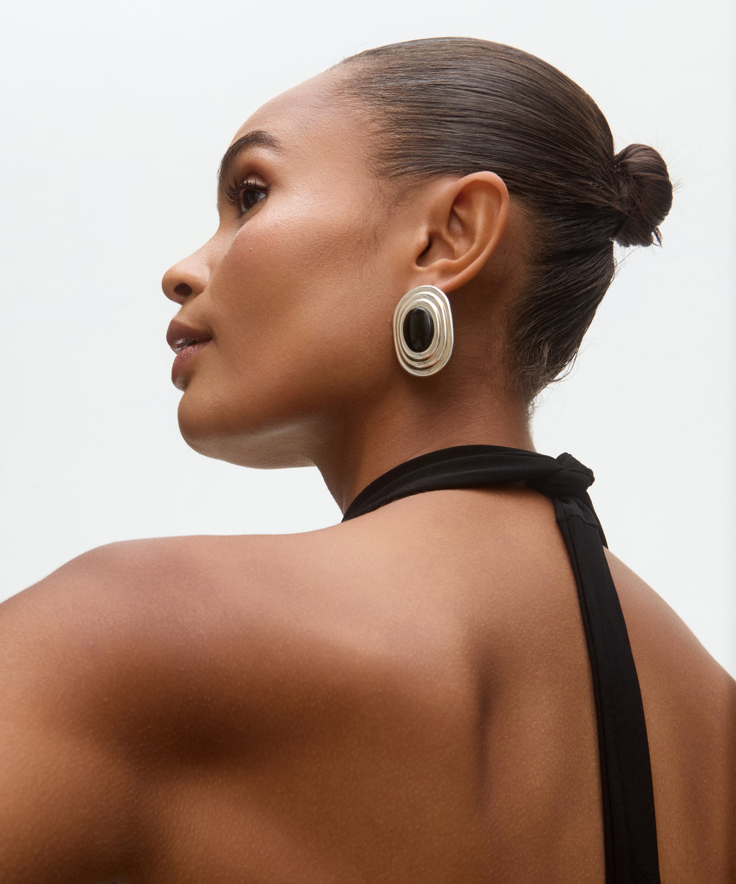 Woman wearing large onyx and silver earrings with a neutral background