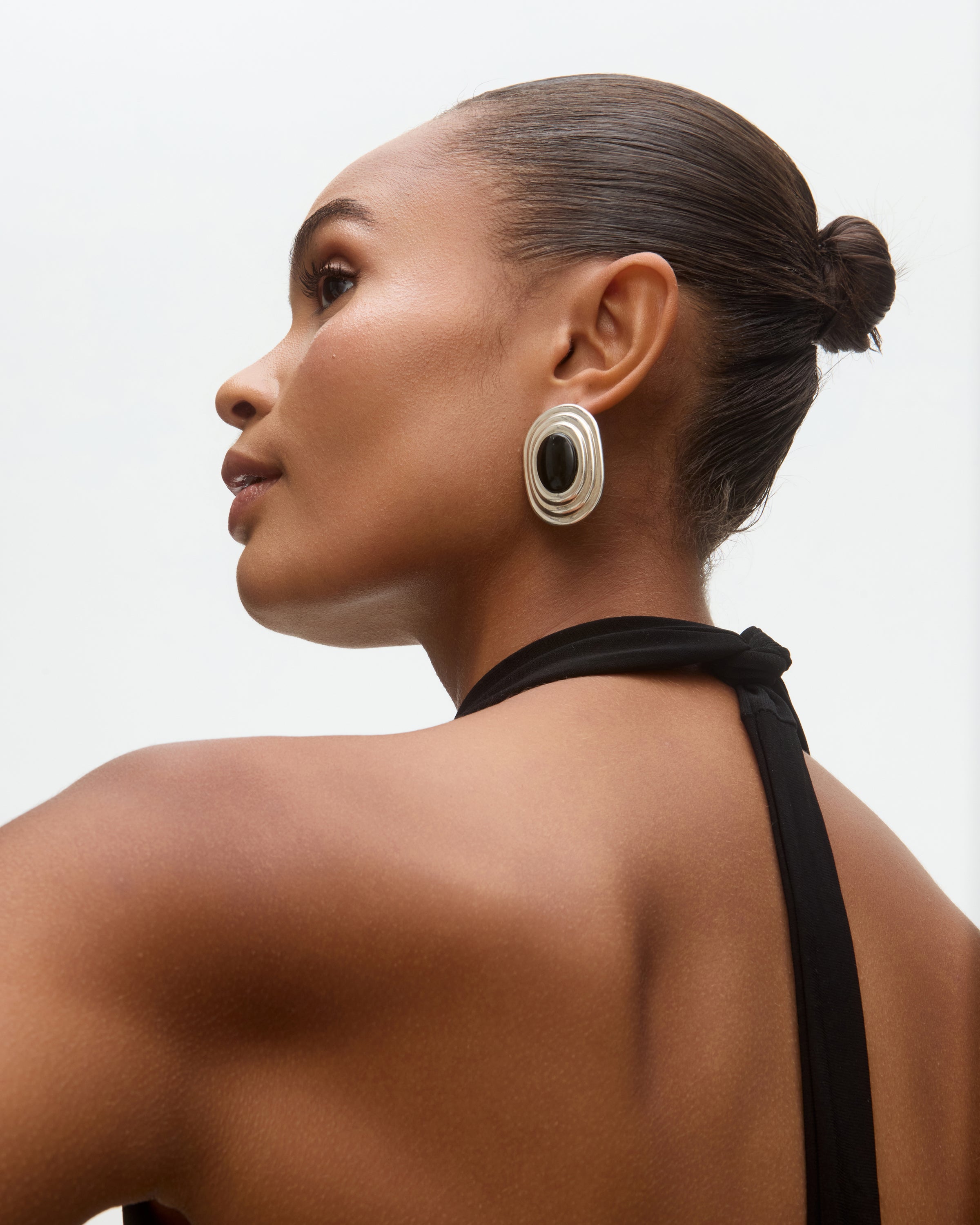 Woman wearing large onyx and silver earrings with a neutral background
