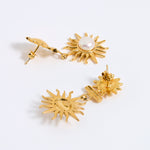 Gold sun-shaped earrings with a central pearl on a white background