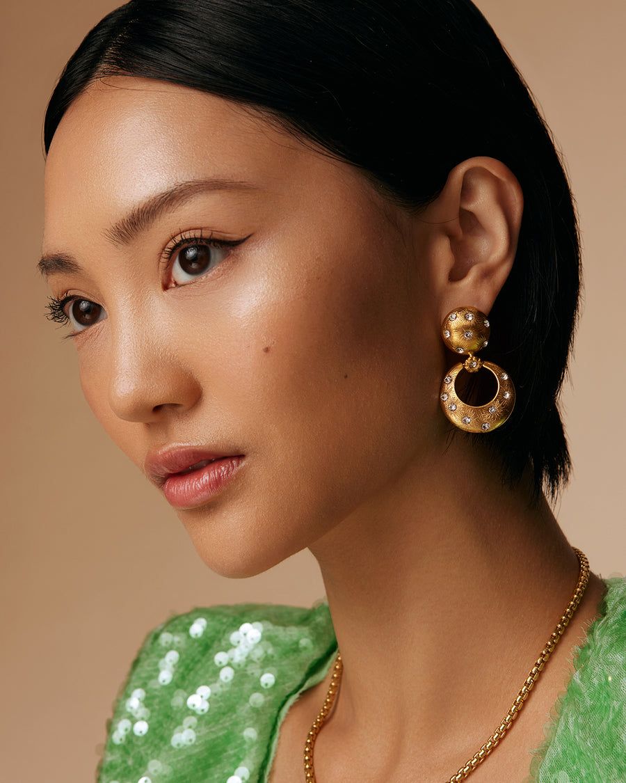 on model shot of chunky gold door knocker style earrings with clear crystal stars etched into the gold plated silver