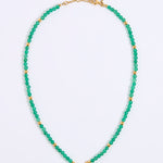 A beaded necklace featuring small, faceted green beads separated by round gold spacer beads, with a gold clasp and extender chain, displayed on a white background.