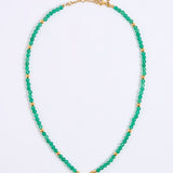A beaded necklace featuring small, faceted green beads separated by round gold spacer beads, with a gold clasp and extender chain, displayed on a white background.