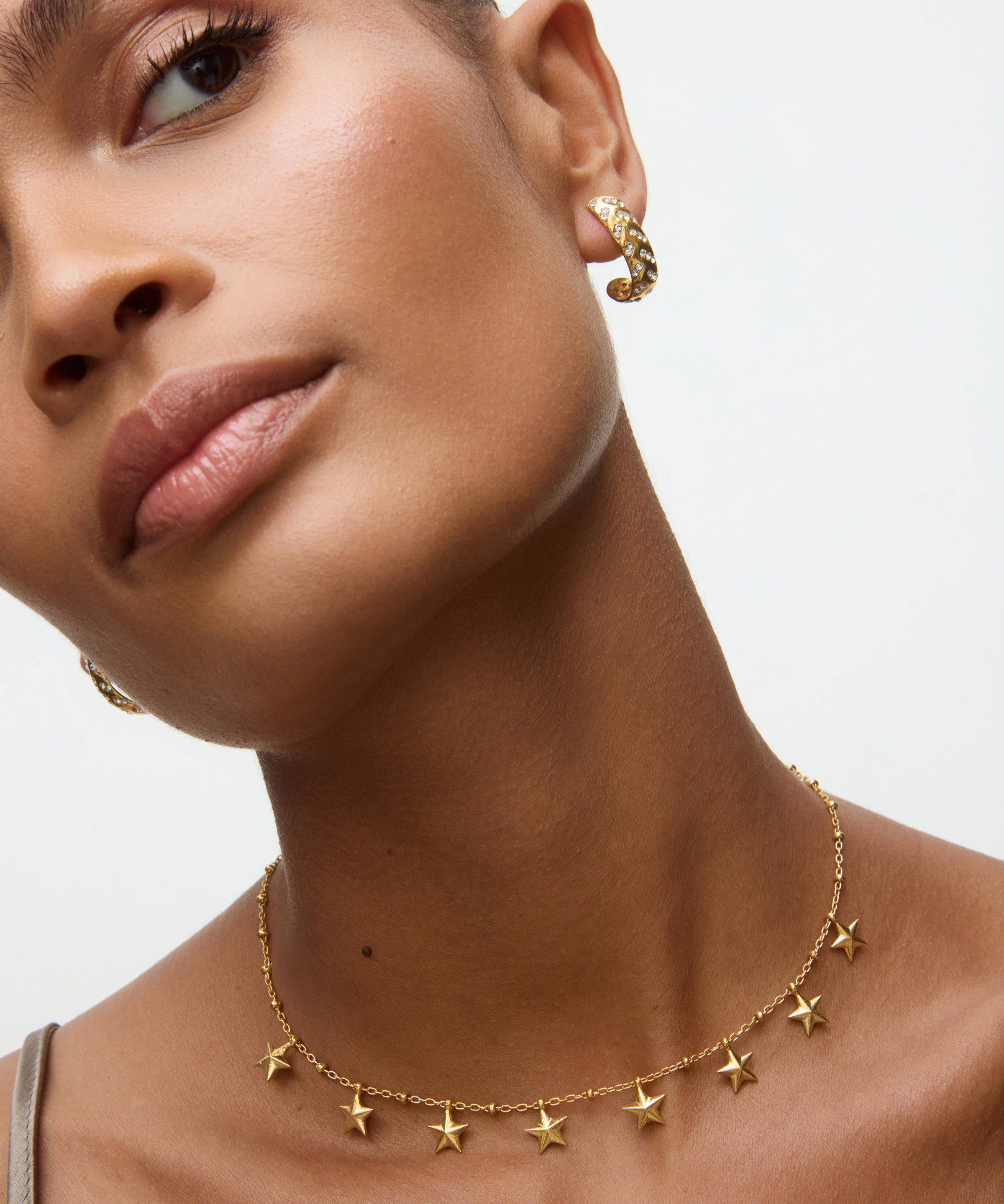 Close-up of a woman wearing gold star-shaped earrings and a necklace on a neutral background