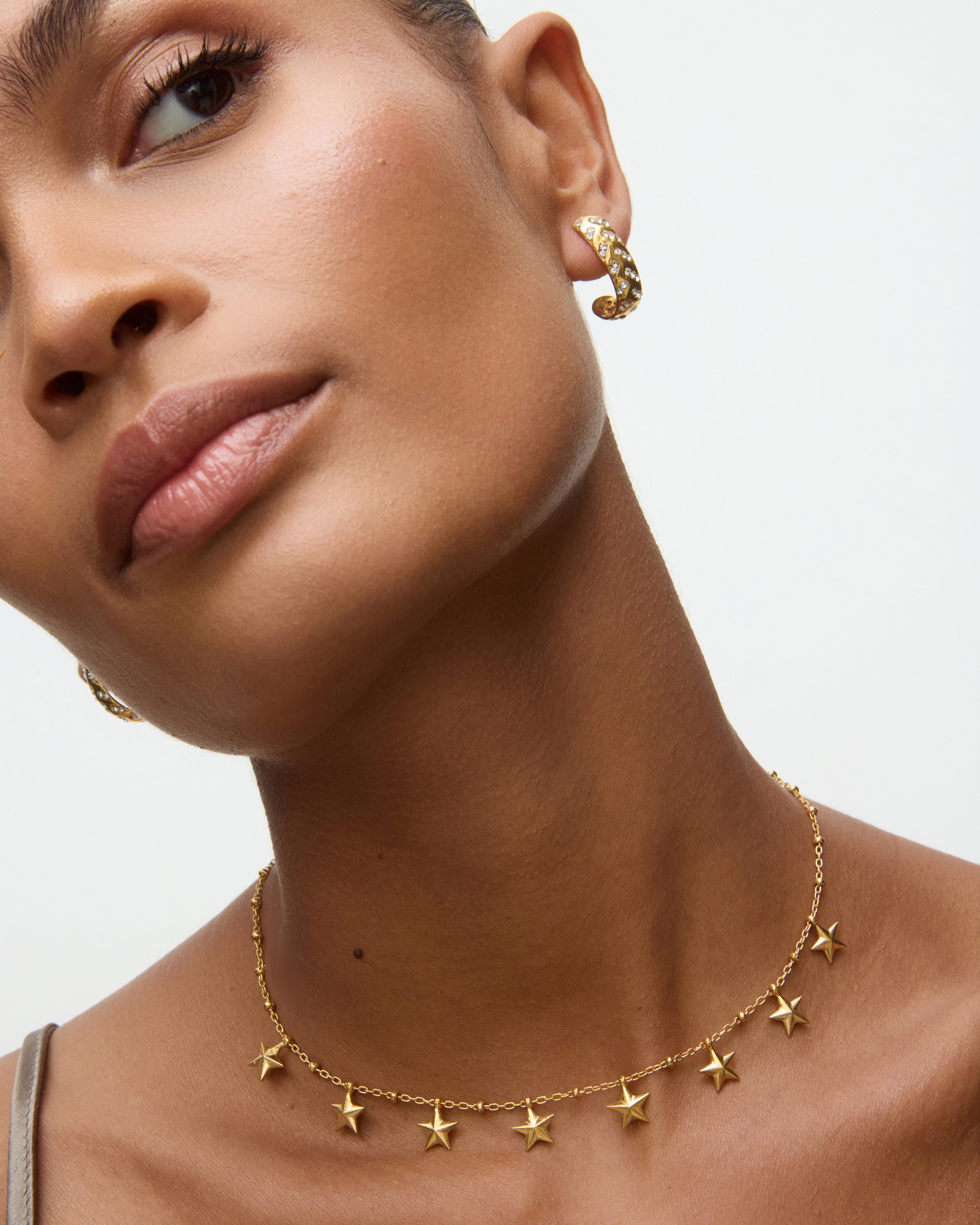 Close-up of a woman wearing gold star-shaped earrings and a necklace on a neutral background