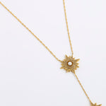 A gold-toned Y-necklace featuring two starburst sun motifs, each detailed with small clear stones and a central white pearl, displayed on a clean white background.