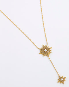 A gold-toned Y-necklace featuring two starburst sun motifs, each detailed with small clear stones and a central white pearl, displayed on a clean white background.