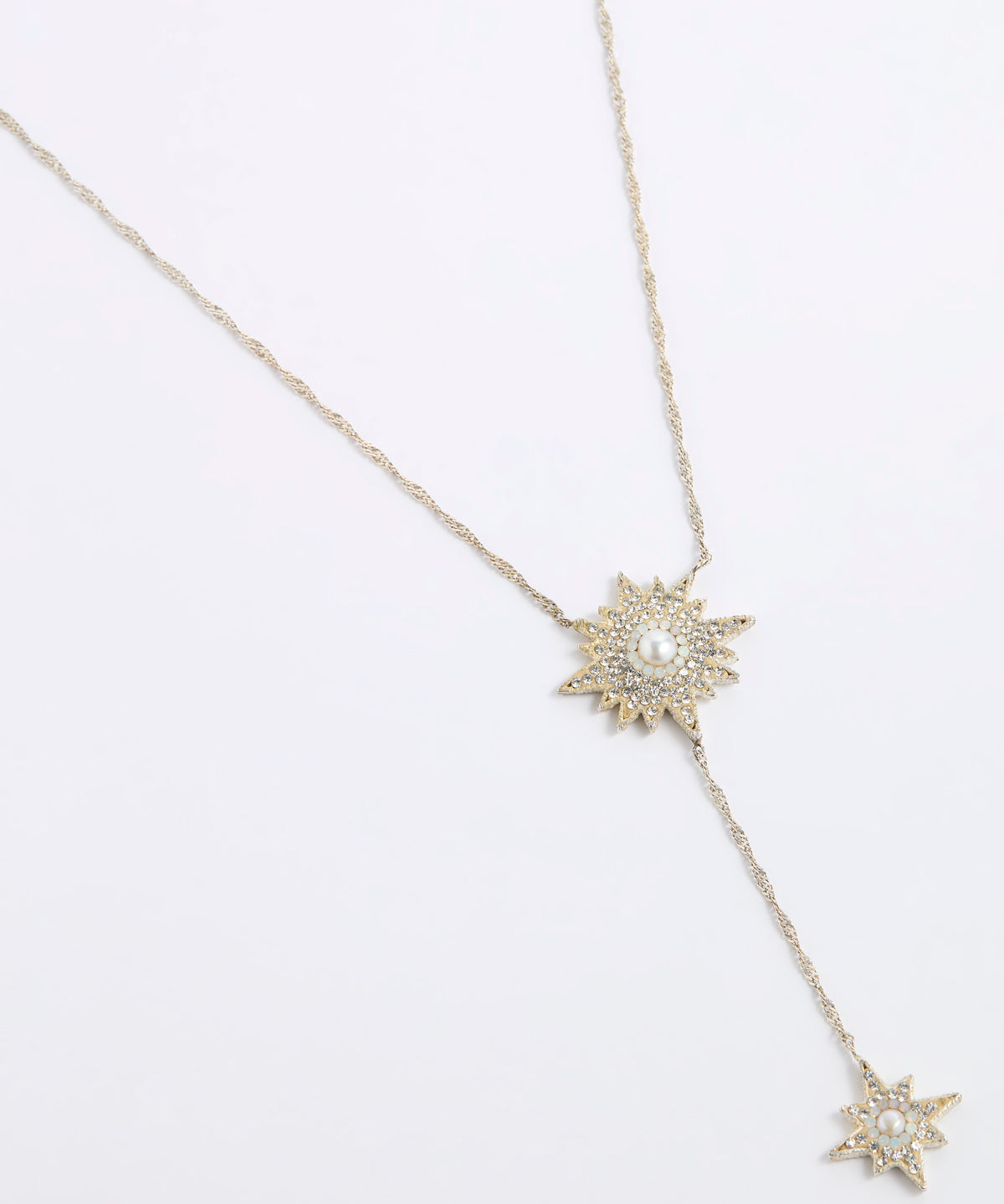 A gold-toned Y-necklace featuring two starburst pendants, each adorned with clear crystals and a central white pearl, displayed on a clean white background.