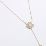 A gold-toned Y-necklace featuring two starburst pendants, each adorned with clear crystals and a central white pearl, displayed on a clean white background.