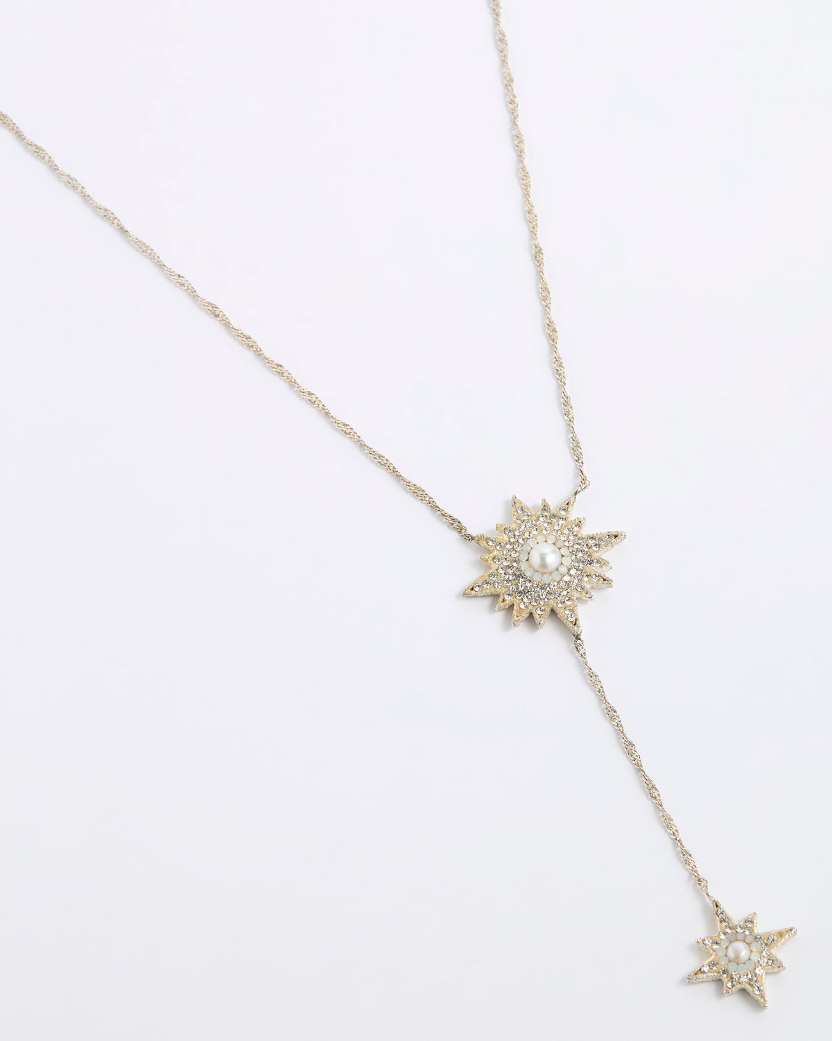 A gold-toned Y-necklace featuring two starburst pendants, each adorned with clear crystals and a central white pearl, displayed on a clean white background.