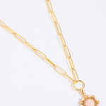 Gold coloured chain necklace with a pink floral pendant on a white background
