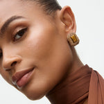 Close-up of a woman wearing gold earrings with a brown top and scarf.