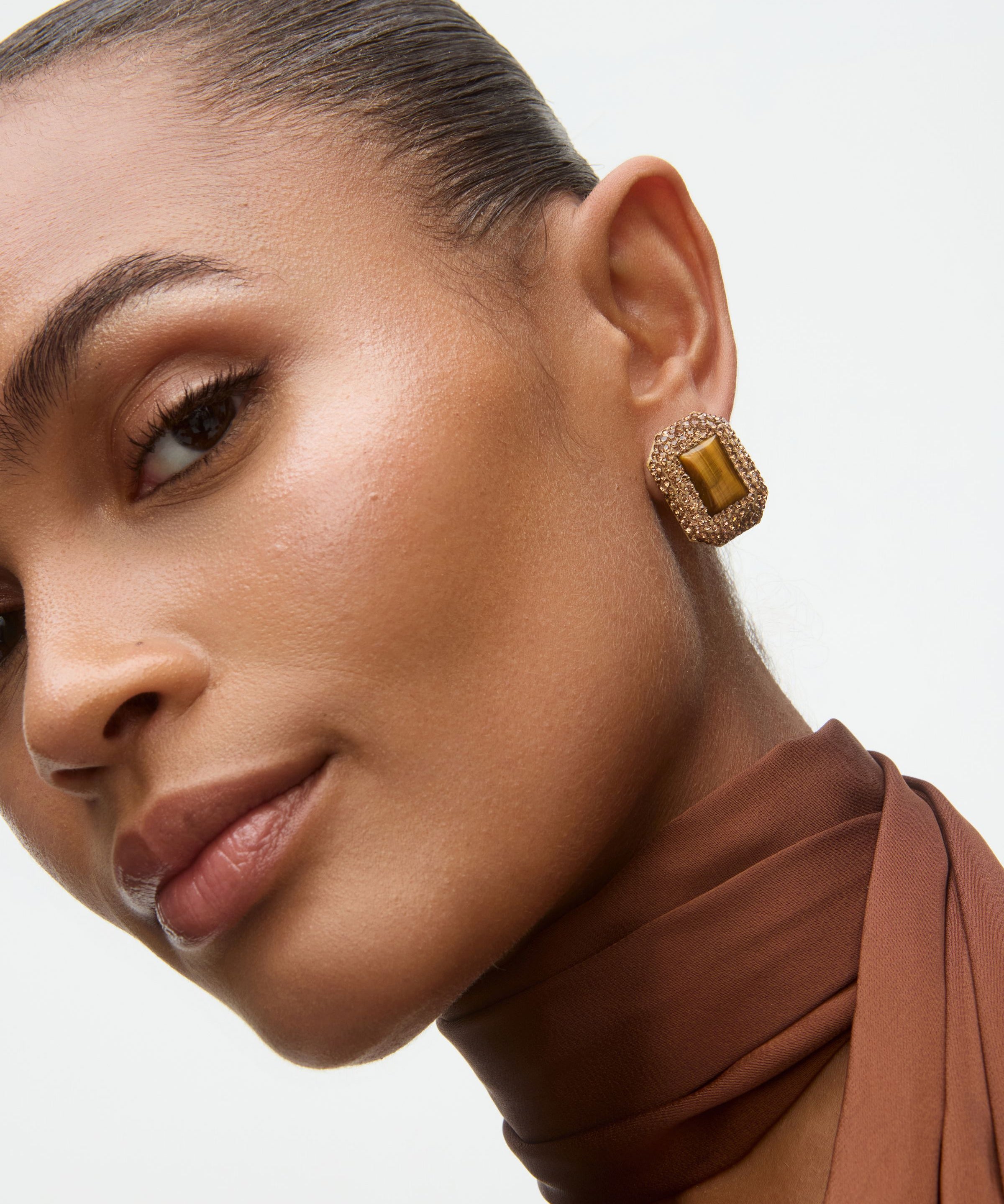 Close-up of a woman wearing gold earrings with a brown top and scarf.
