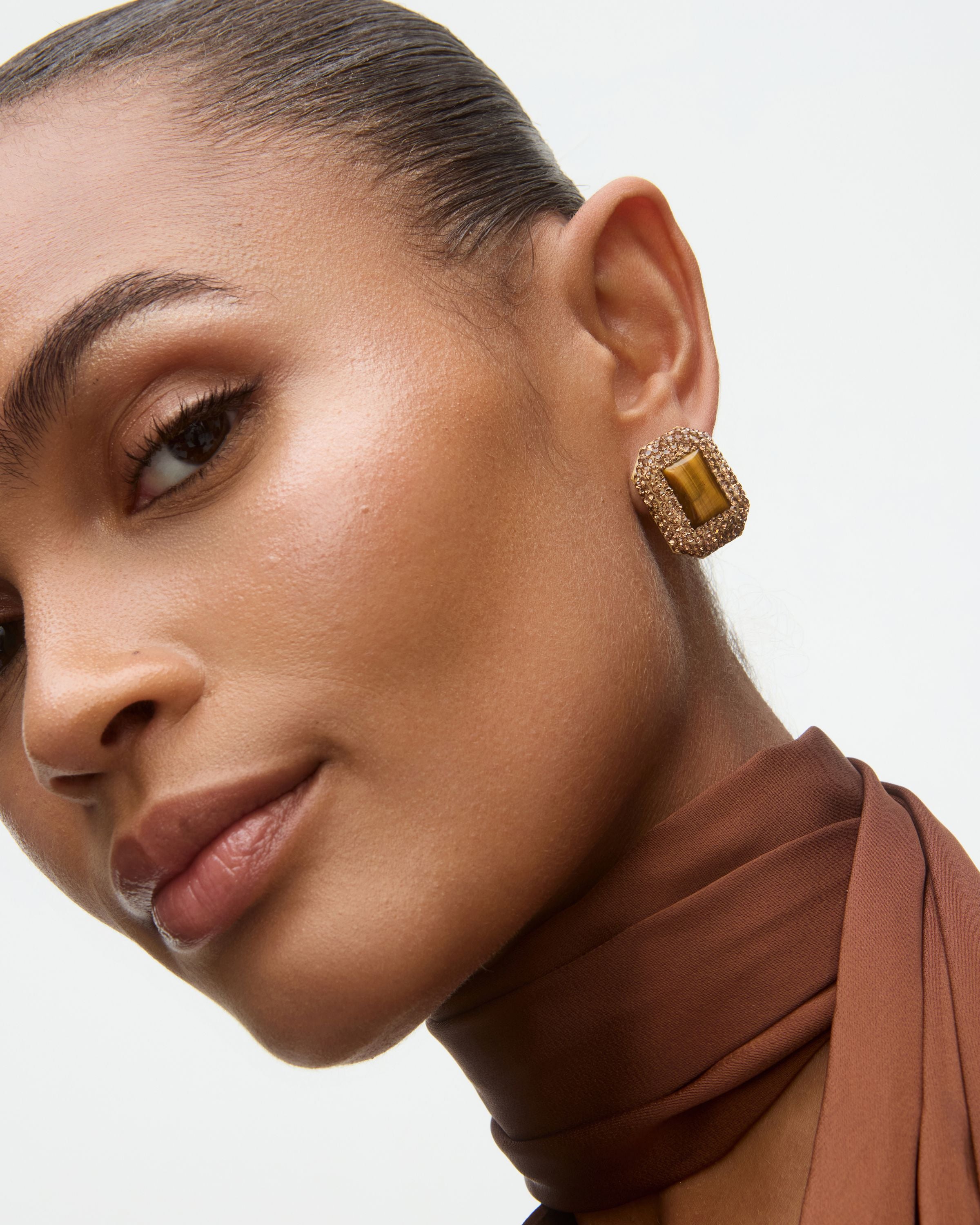 Close-up of a woman wearing gold earrings with a brown top and scarf.