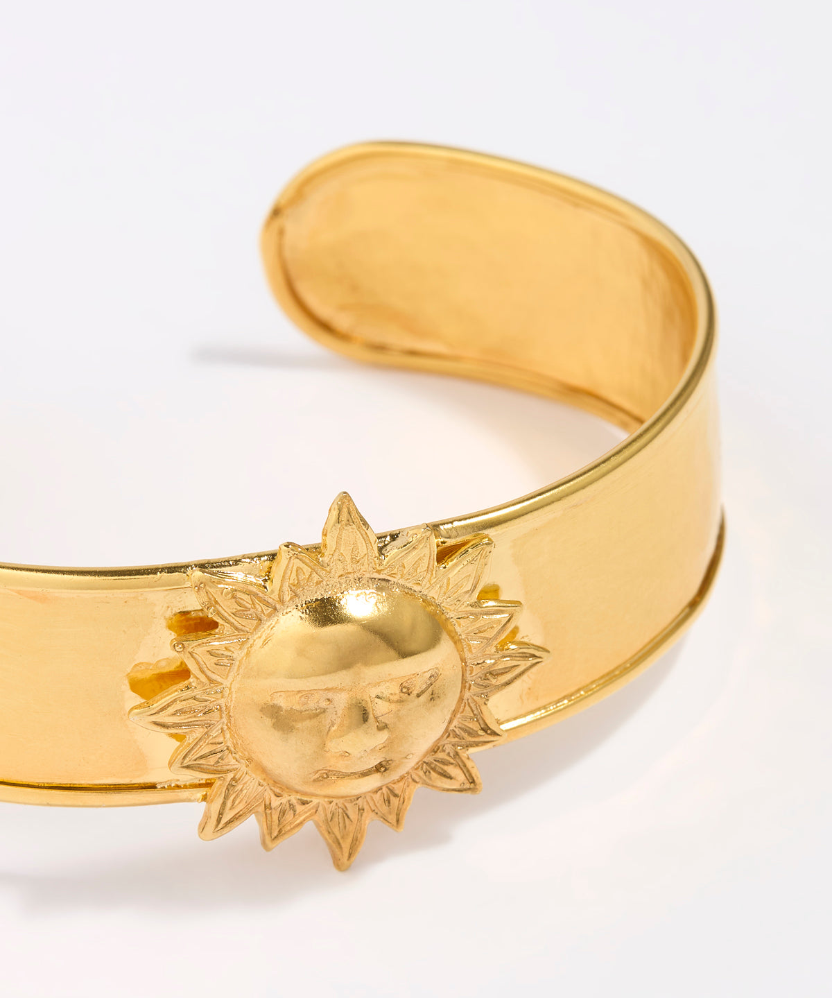 Gold coloured cuff bracelet with sun design on a white background