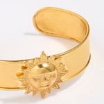Gold coloured cuff bracelet with sun design on a white background
