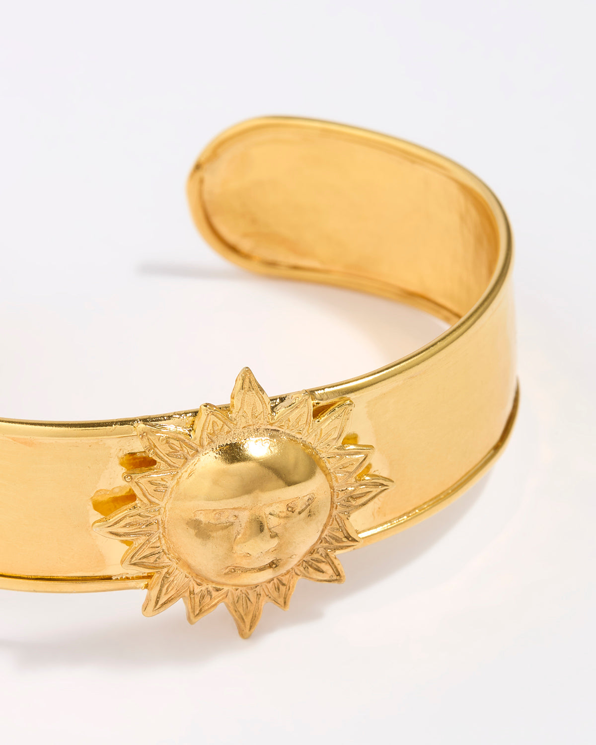 Gold coloured cuff bracelet with sun design on a white background