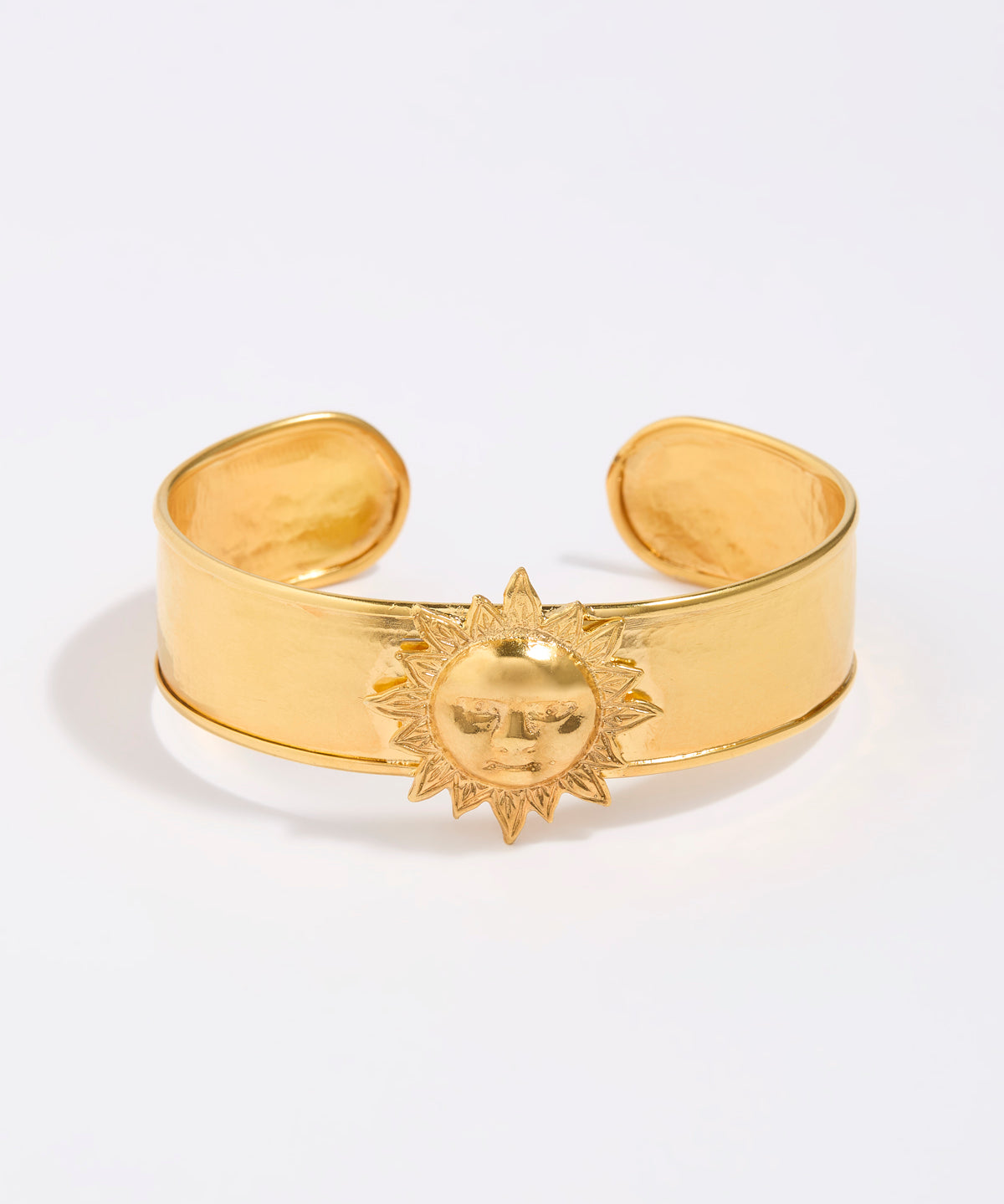 Gold cuff bracelet with sun design on a white background