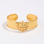 Gold cuff bracelet with sun design on a white background