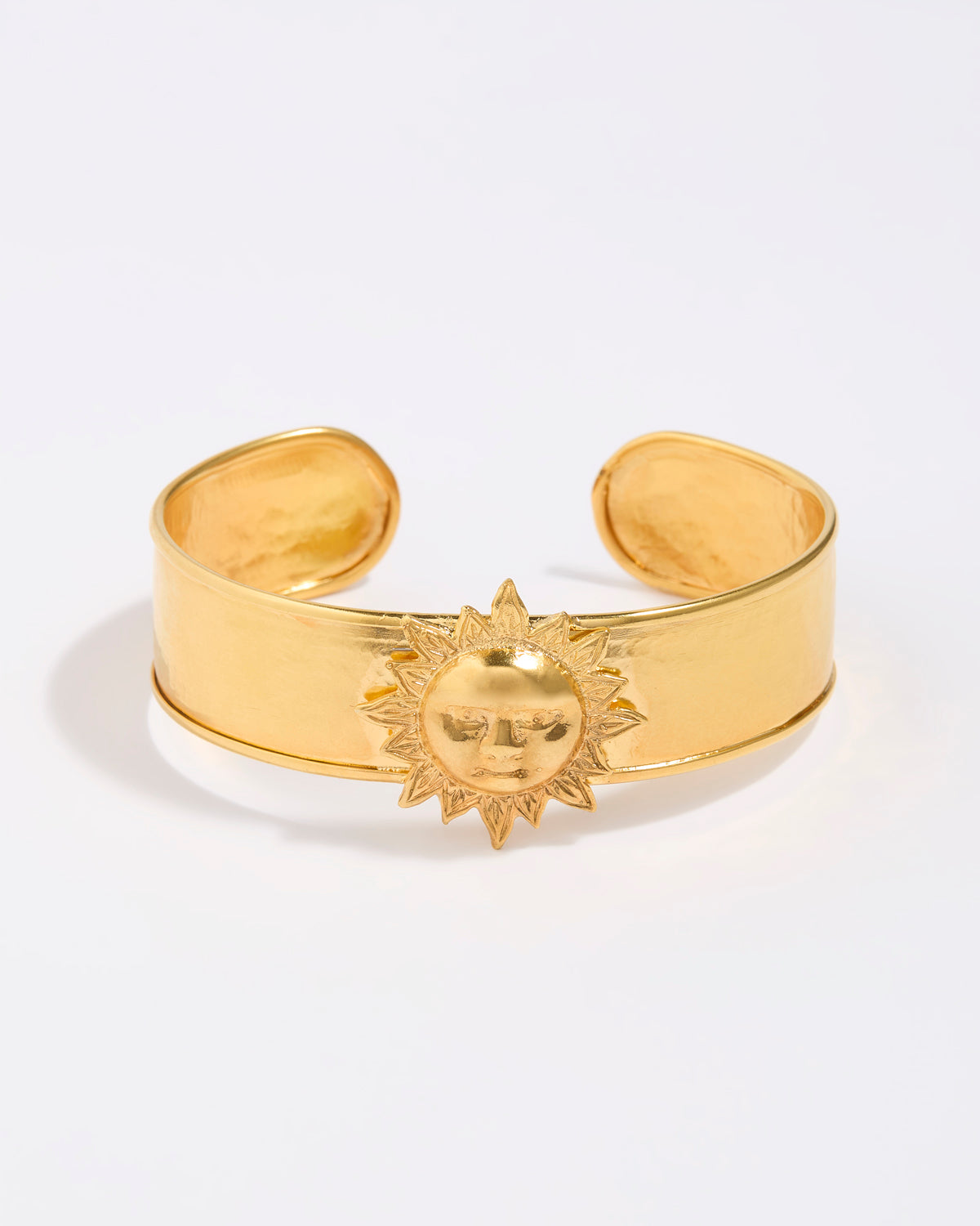 Gold cuff bracelet with sun design on a white background