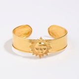Gold cuff bracelet with sun design on a white background