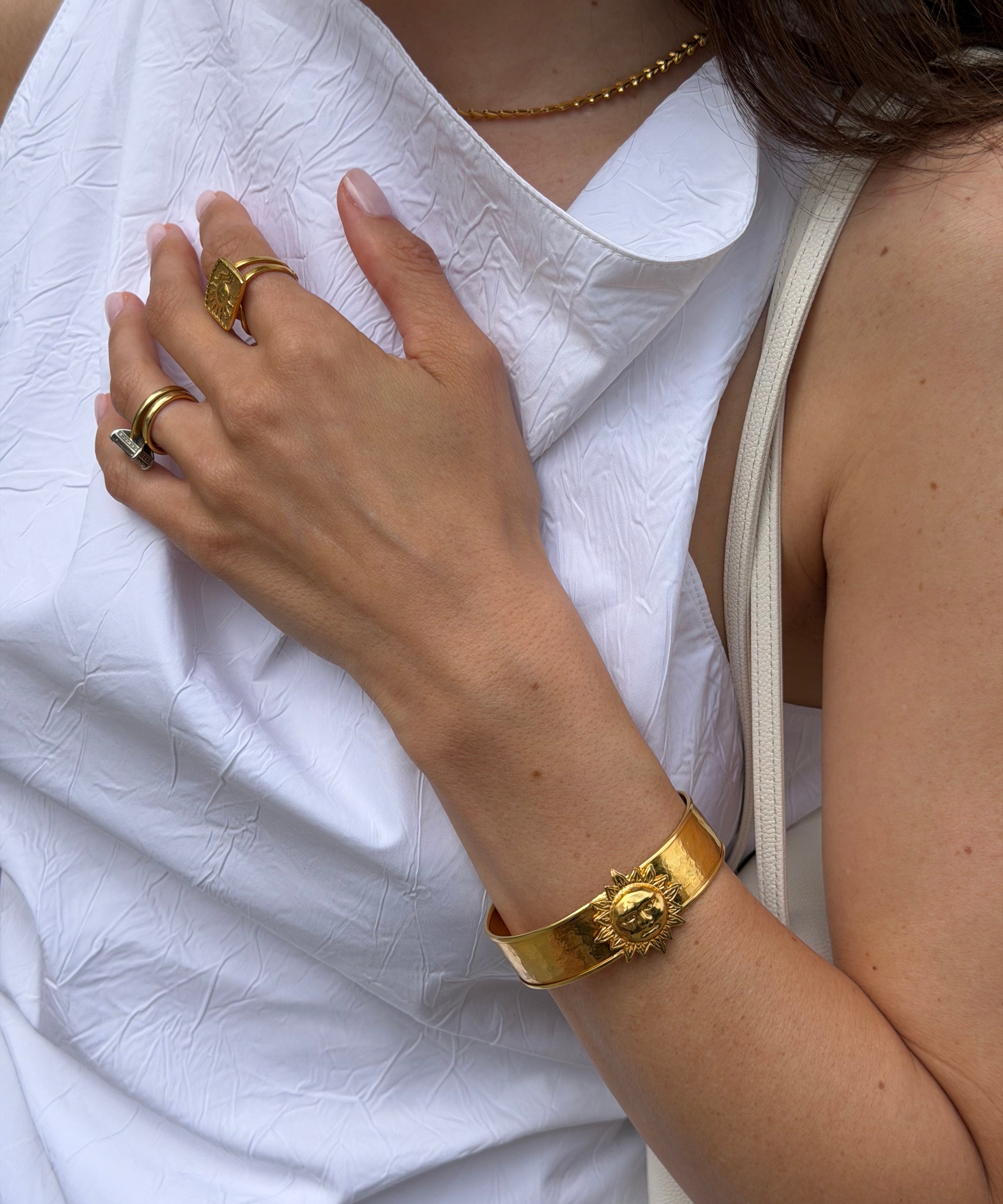 Close-up of a person wearing gold sun cuff bracelet on a white fabric background
