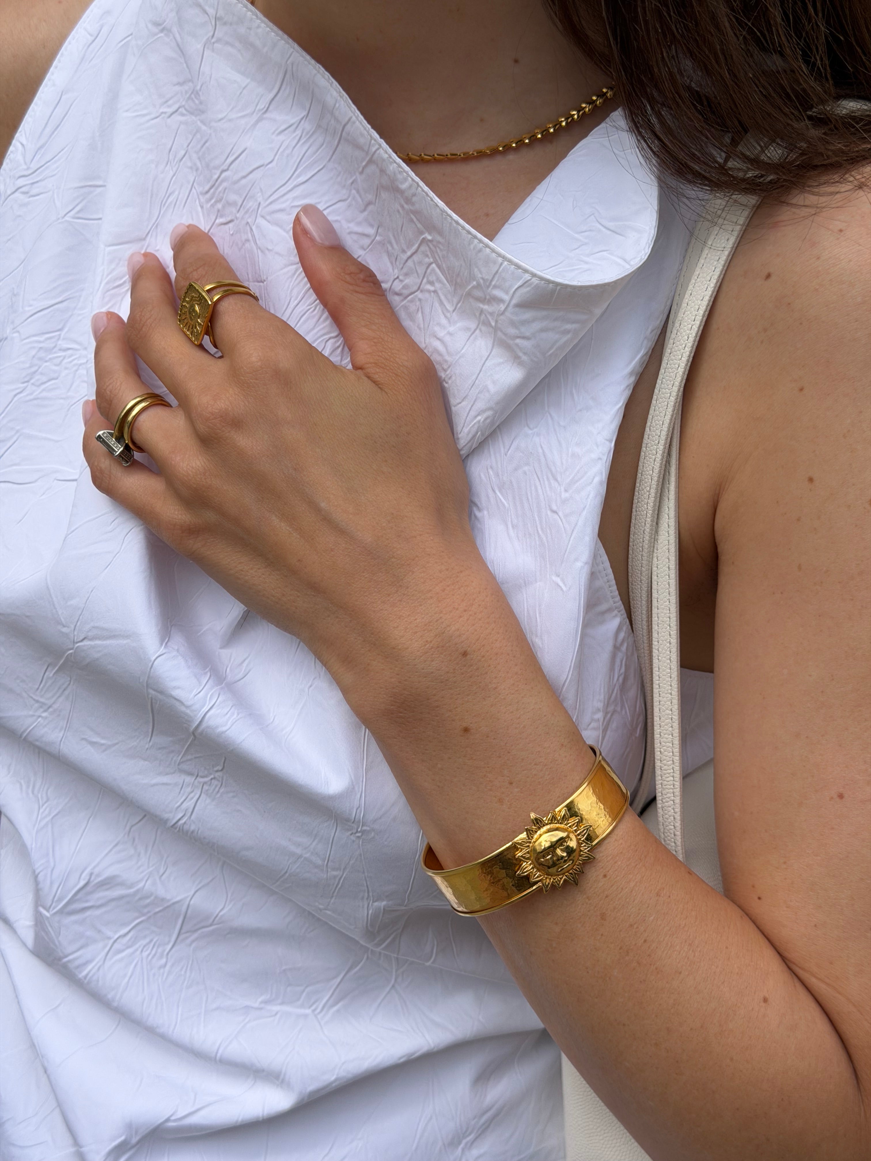 Close-up of a person wearing gold sun cuff bracelet on a white fabric background