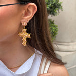 Close-up of a person wearing gold cross earrings 