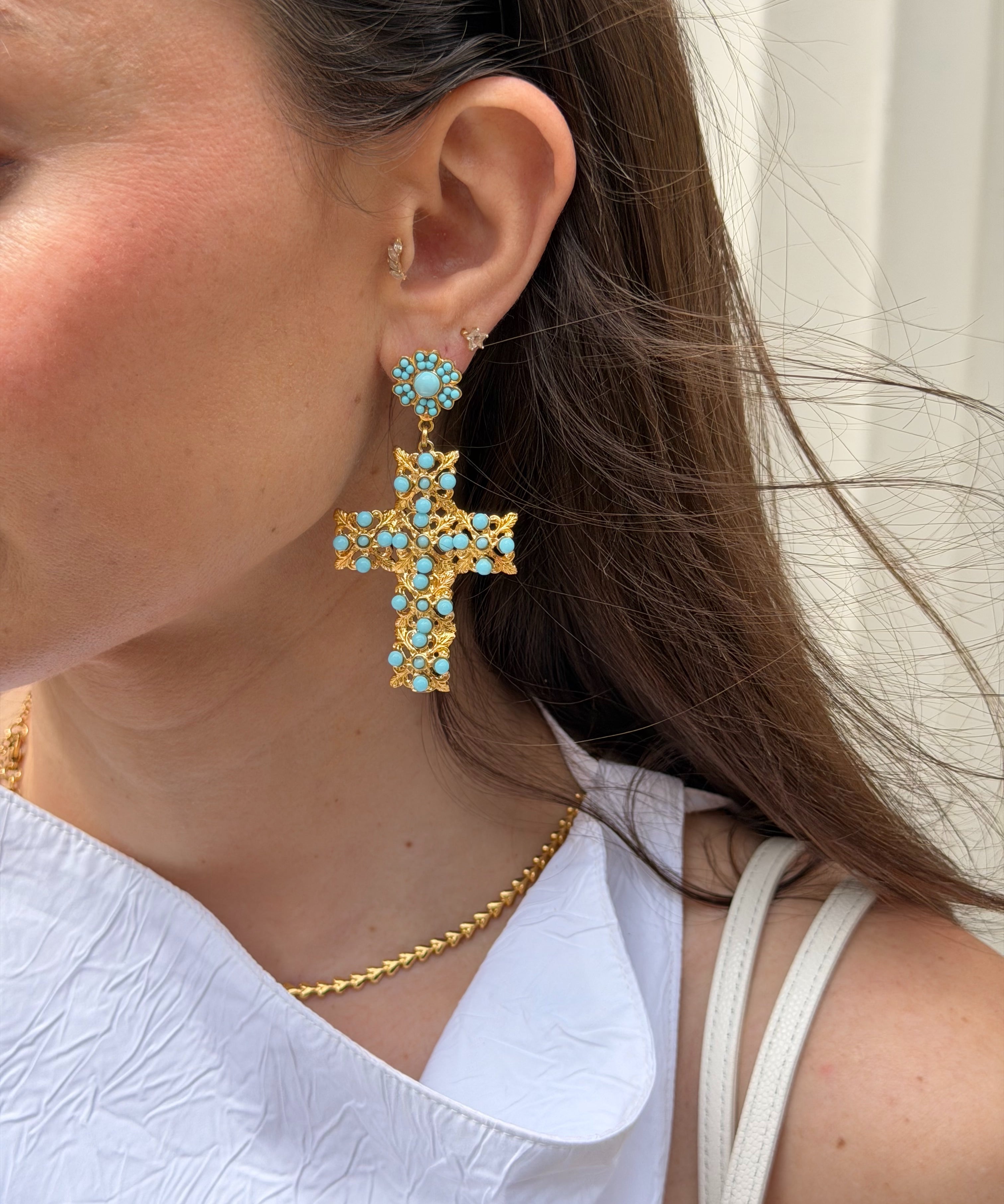 Close-up of a person wearing gold cross earrings with turquoise stones.