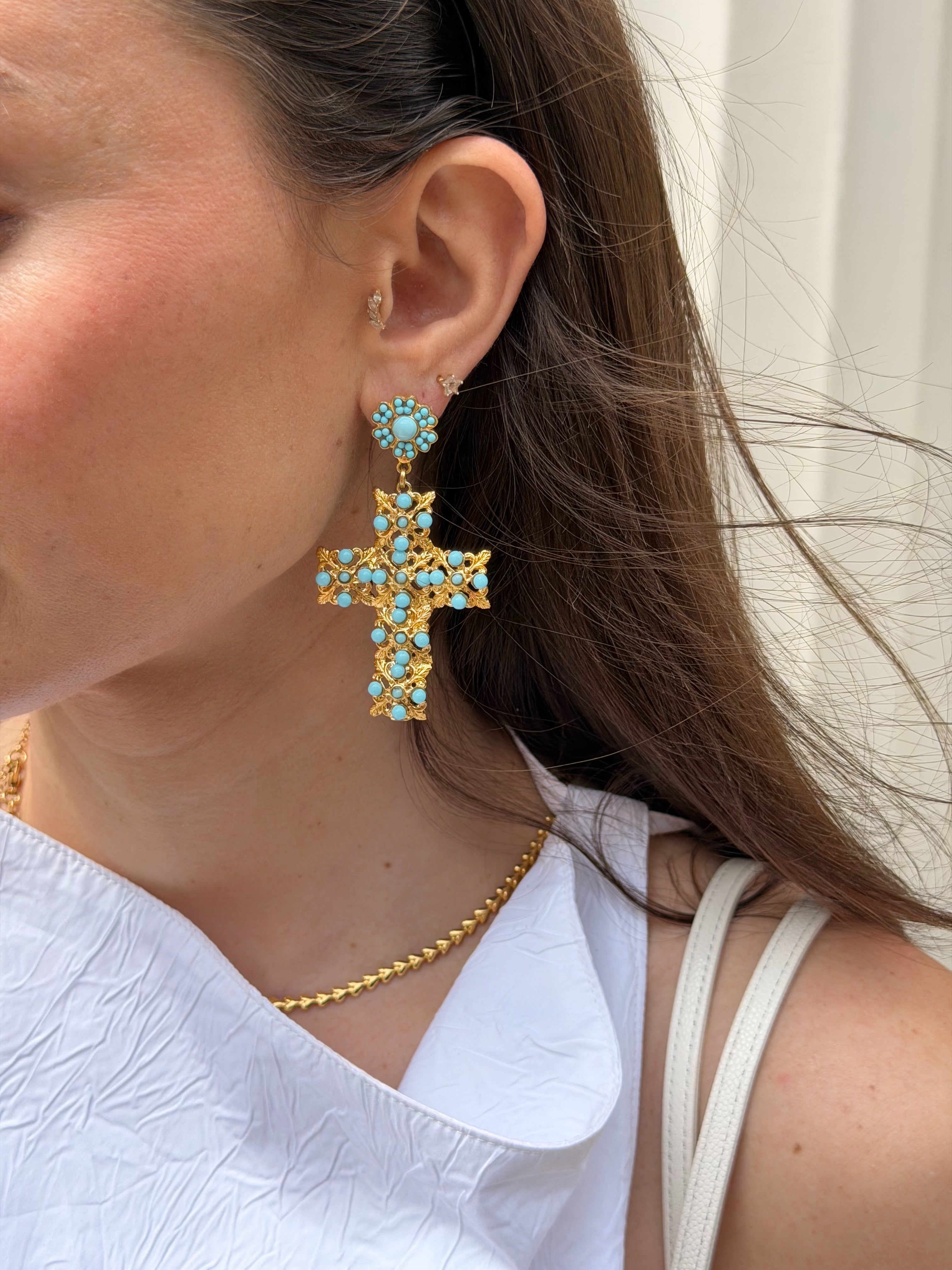 Close-up of a person wearing gold cross earrings with turquoise stones.