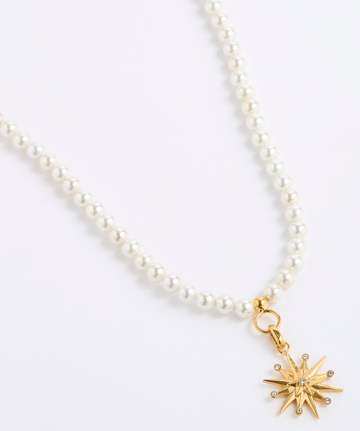 A white pearl necklace featuring a gold 12-pointed star charm pendant, embellished with sparkling clear crystals, presented on a white background.
