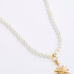 A white pearl necklace featuring a gold 12-pointed star charm pendant, embellished with sparkling clear crystals, presented on a white background.