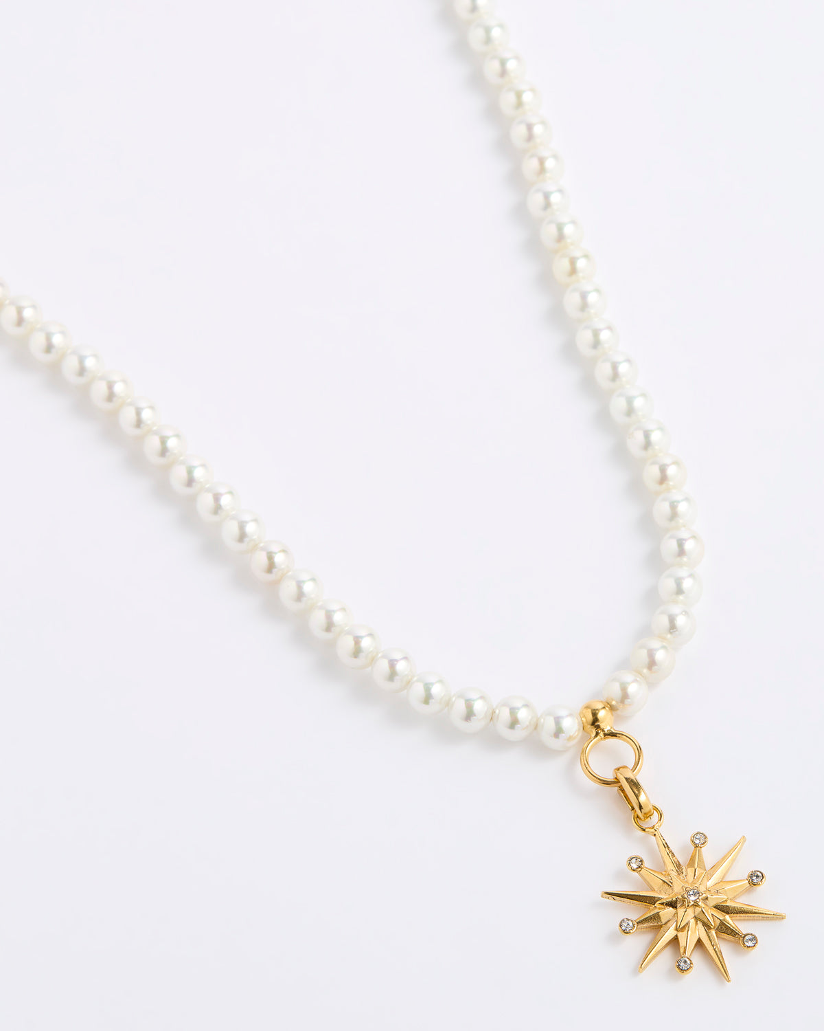 A white pearl necklace featuring a gold 12-pointed star charm pendant, embellished with sparkling clear crystals, presented on a white background.