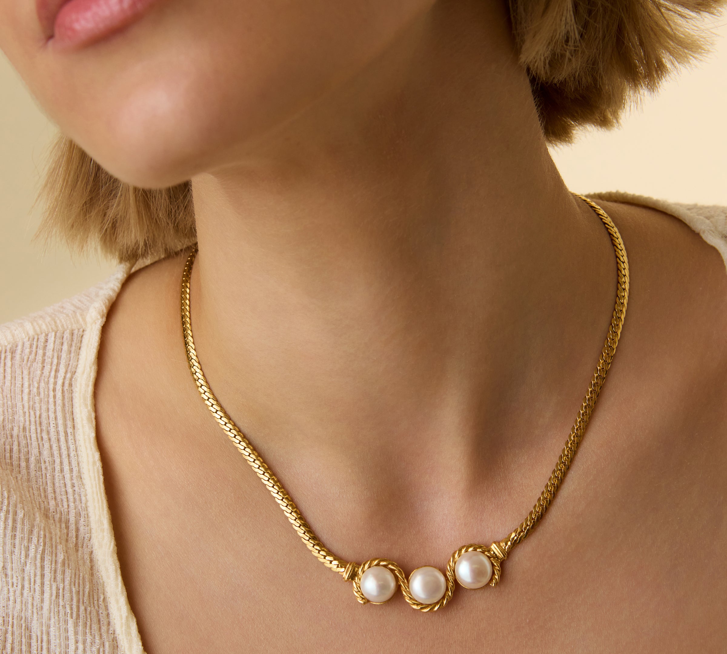 Close-up of a model wearing a gold plated trio pearl necklace on a neutral background.