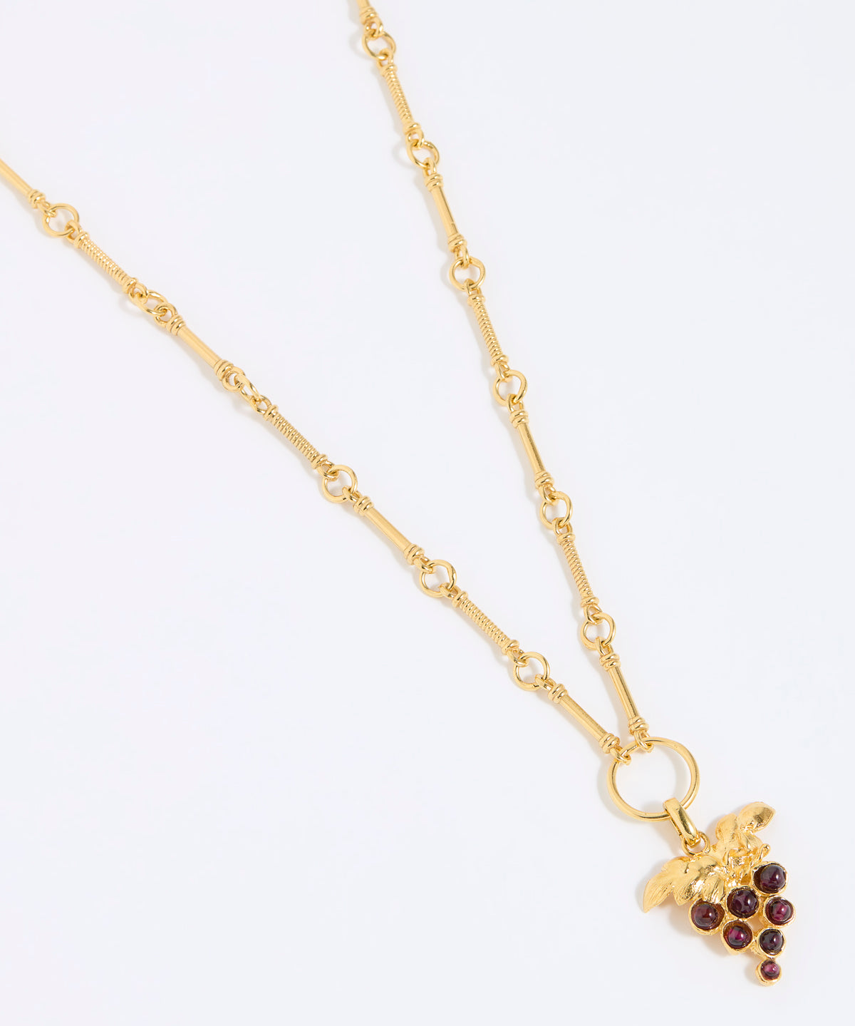 Gold coloured necklace with a grape charm on a white background