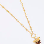 Gold coloured necklace with a grape charm on a white background