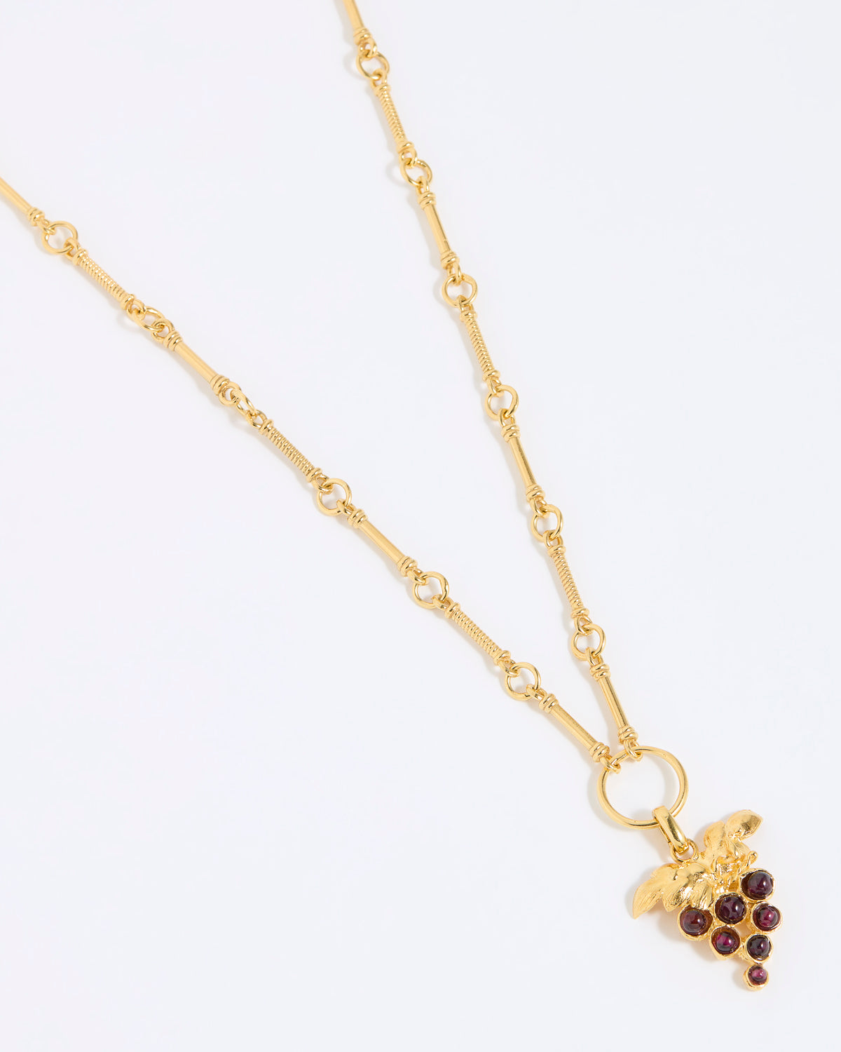 Gold coloured necklace with a grape charm on a white background