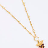 Gold coloured necklace with a grape charm on a white background