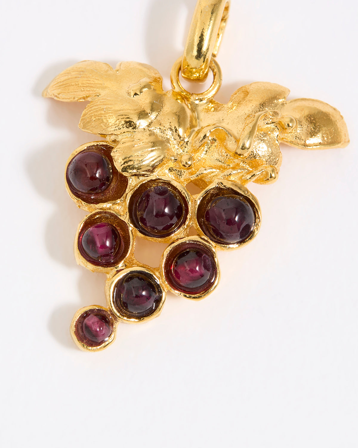 Gold pendant with red gemstones in the shape of a grape vine on a white background