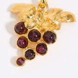 Gold pendant with red gemstones in the shape of a grape vine on a white background
