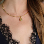 A close-up of a model wearing a delicate gold bangle necklace with a small green pendant, paired with a black lace top.