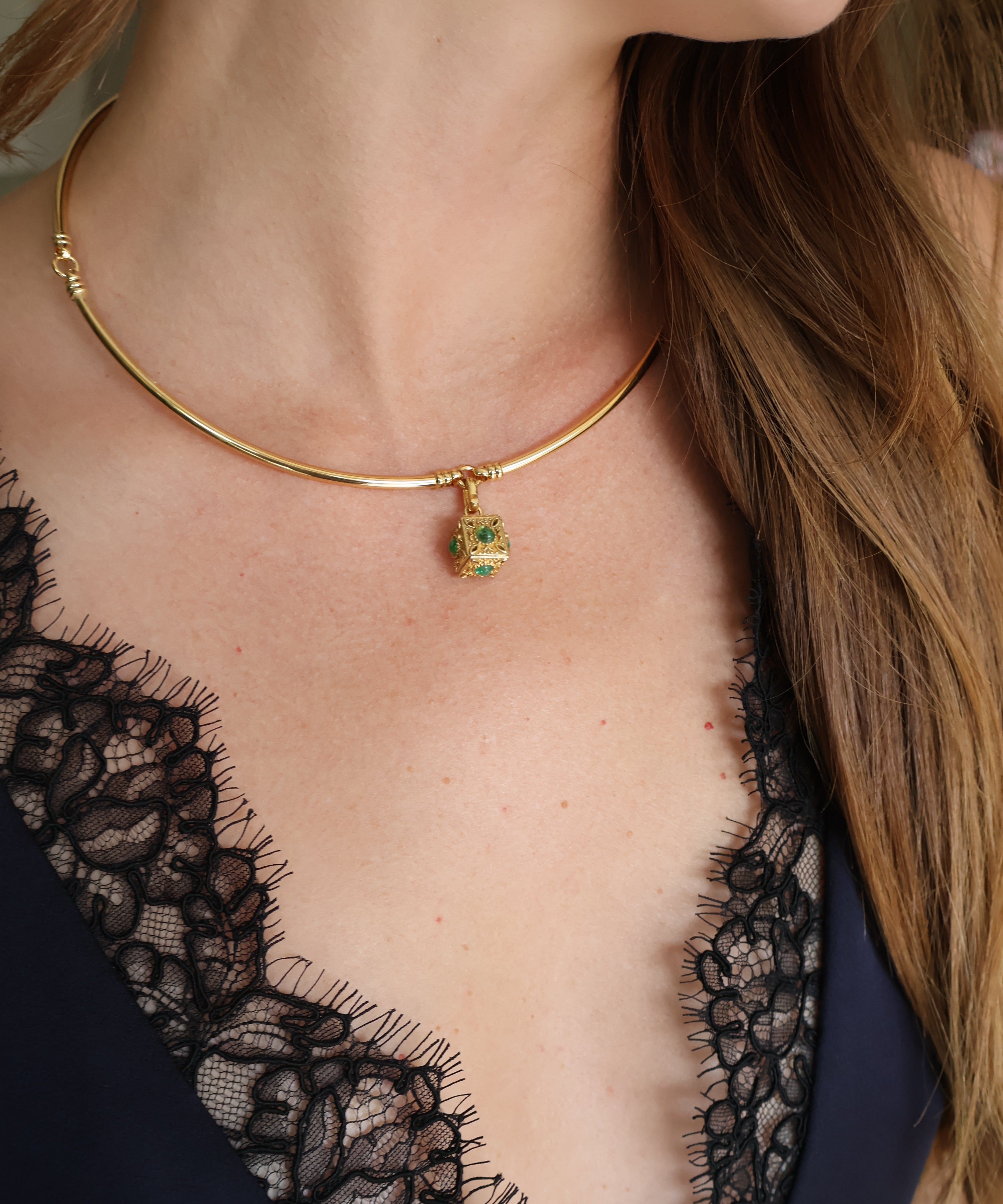 A close-up of a model wearing a delicate gold bangle necklace with a small green pendant, paired with a black lace top.