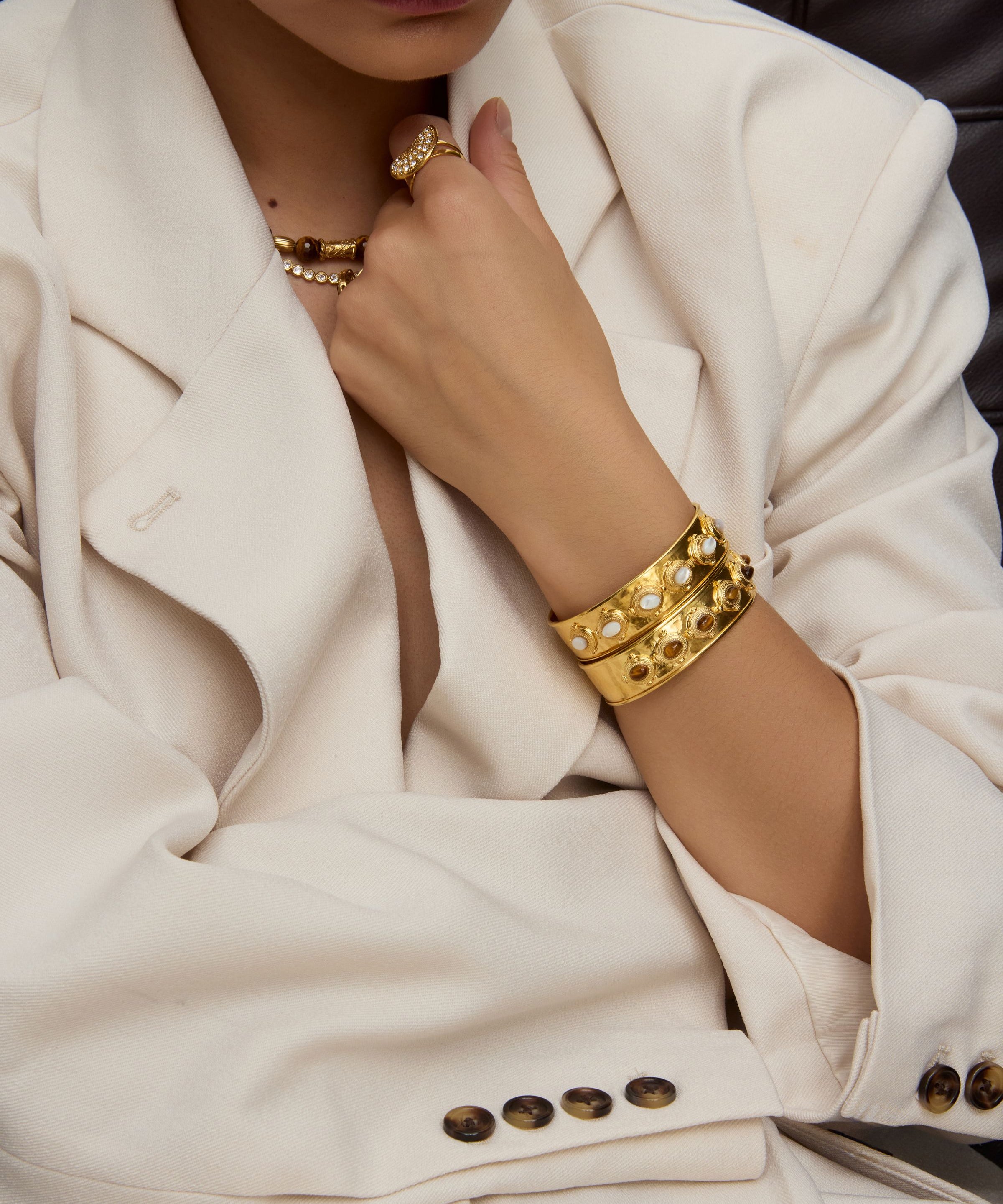 Person wearing gold jewelry including a bracelet and necklace, with a focus on the arm and hand.