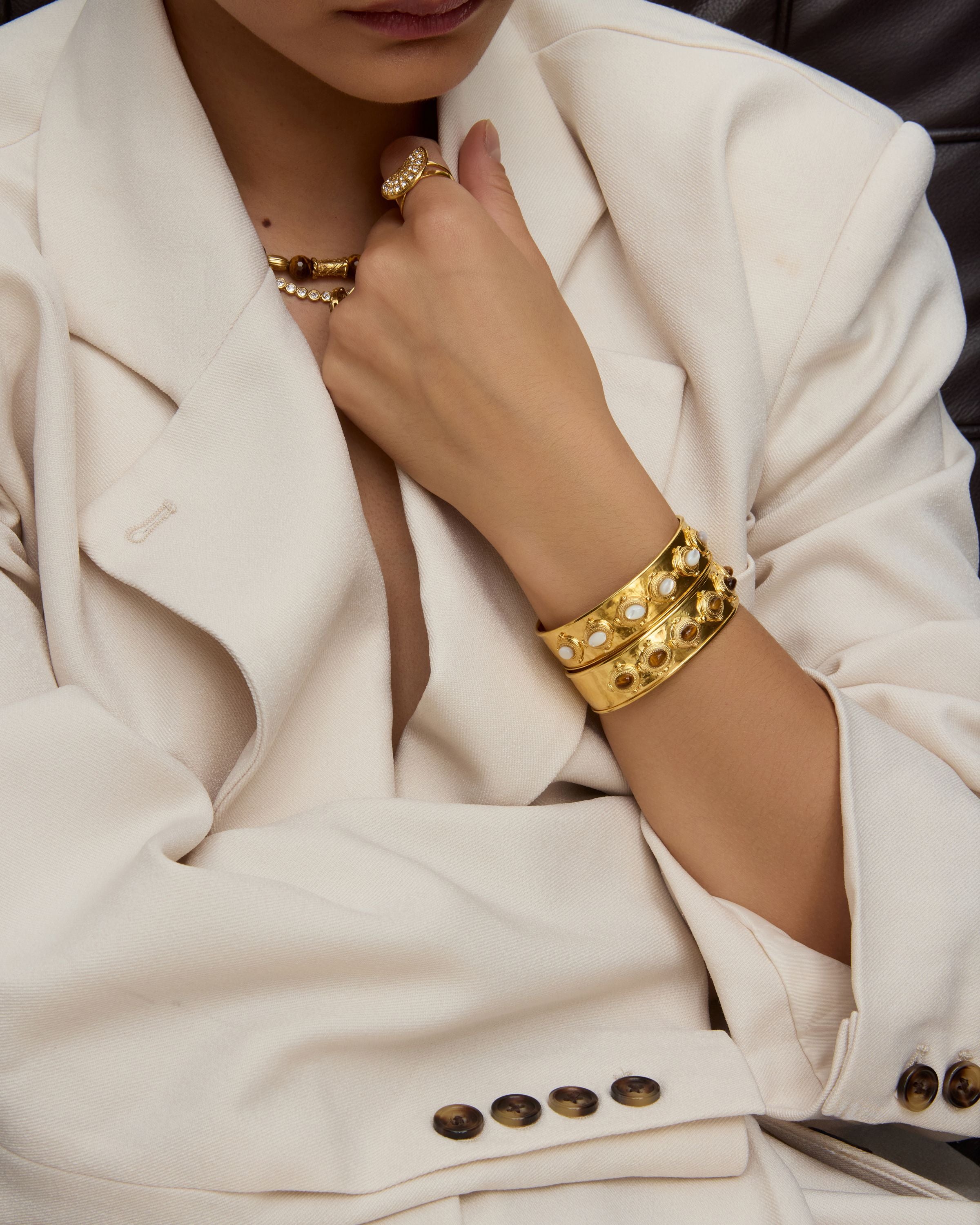 Person wearing gold jewelry including a bracelet and necklace, with a focus on the arm and hand.