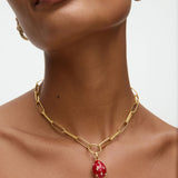 Gold chain necklace with a red egg shaped pendant worn by a model on a neutral background