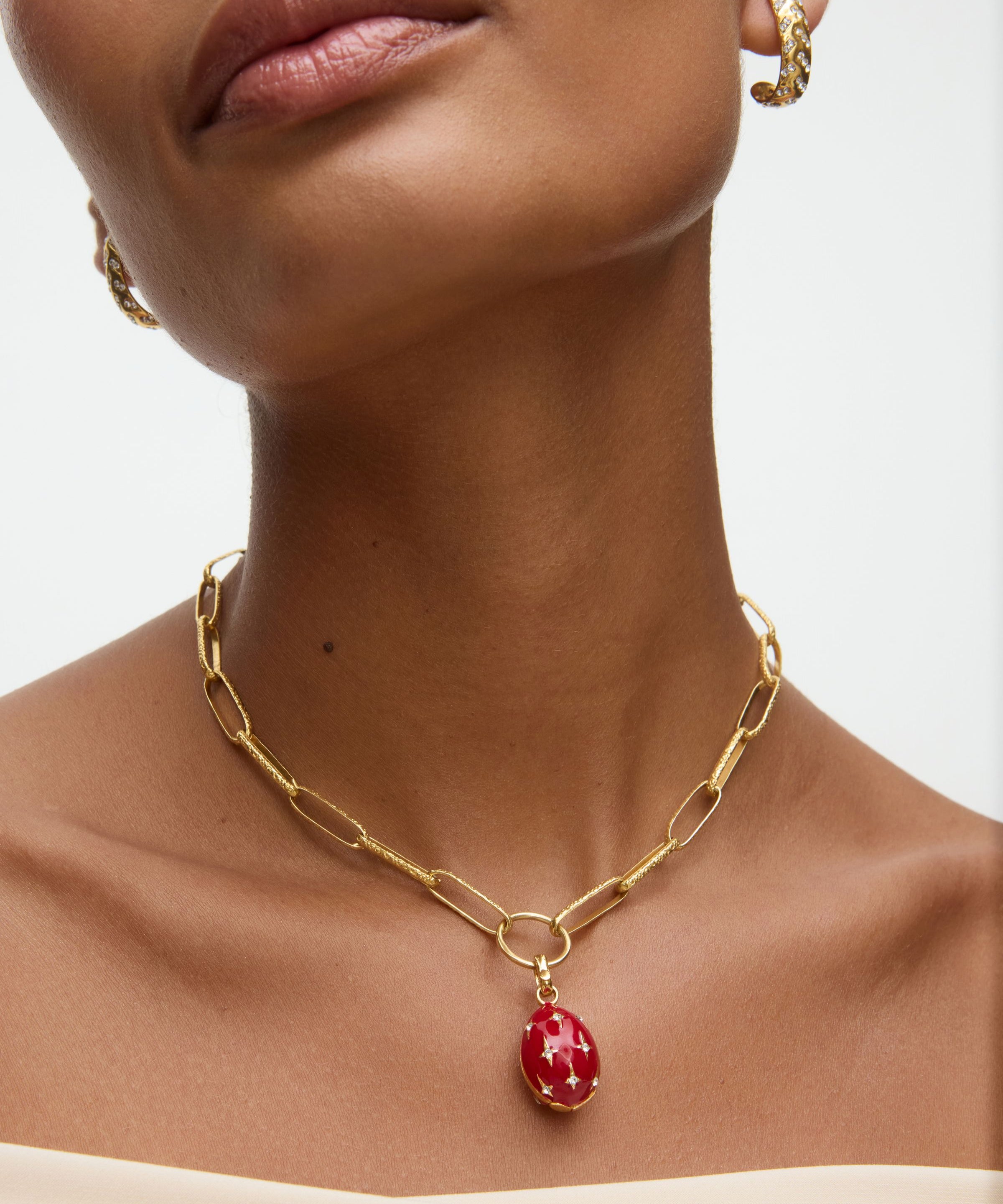 Gold chain necklace with a red egg shaped pendant worn by a model on a neutral background