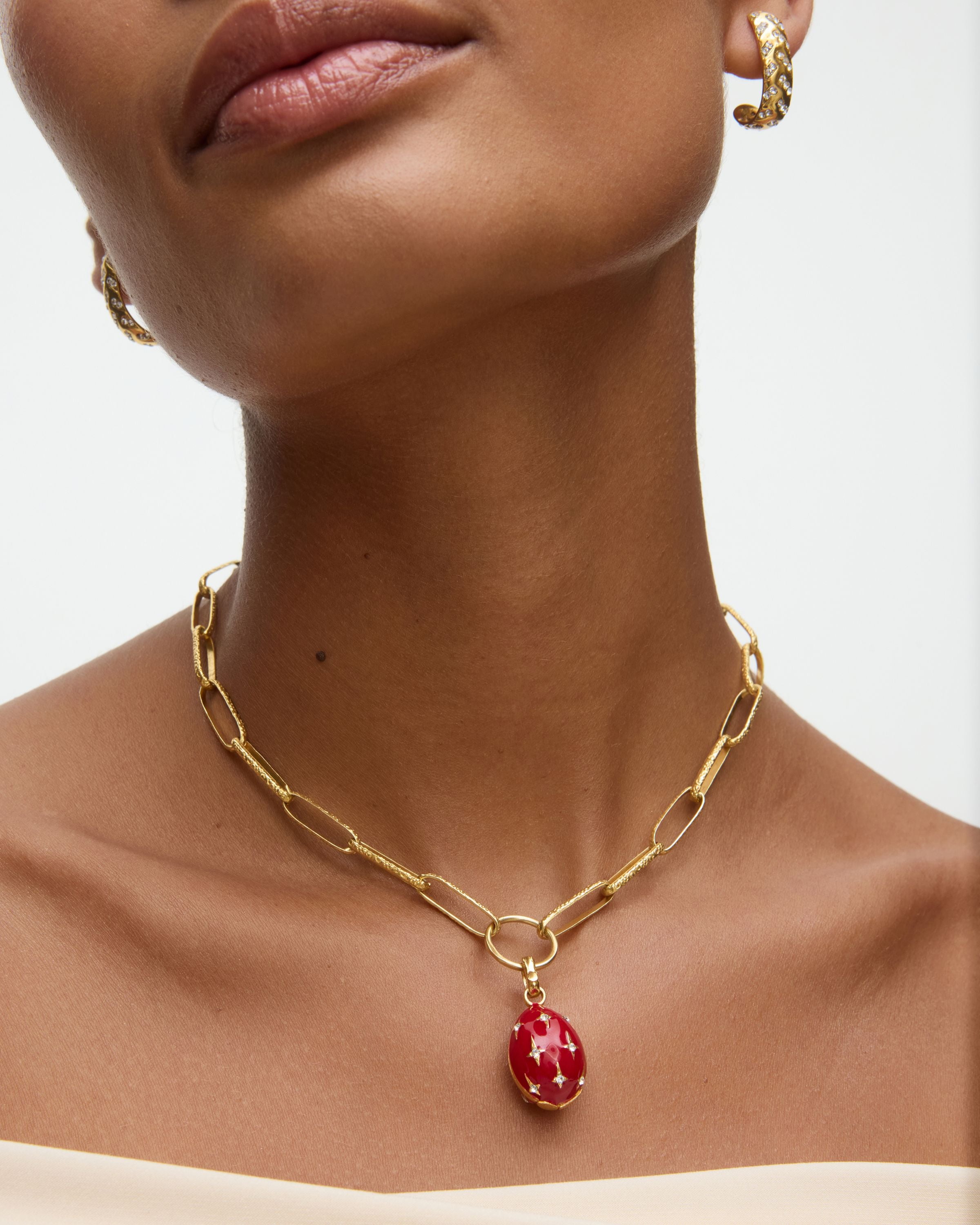 Gold chain necklace with a red egg shaped pendant worn by a model on a neutral background