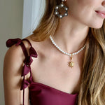 woman wearing statement hoop earrings embellished with black crystals and pearls and a pearl necklace with a 12 pointed star charm. 