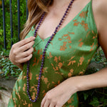 woman wearing a strappy green dress and a long beaded purple necklace 